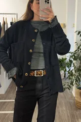 Saco tejido de punto en color negro, con cuello redondo, cierre frontal de botones y bolsillos delanteros aplicados. Presenta puños y ruedo acanalados.