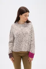 Sweater de tejido de punto con efecto jaspeado, corte holgado y cuello redondo. Presenta mangas largas con puños en contraste de color, uno en tono oscuro y otro en tono rojizo.