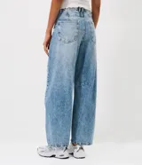 Pantalón de jean con corte barrel, de tiro medio y piernas anchas. Presenta un lavado marmorizado, trabillas en la cintura, cierre frontal con botón y cremallera, bolsillos funcionales y recortes decorativos en las rodillas.