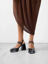 Zapato de tacón negro charol con plataforma, pulsera con dos tiras delanteras con cierre de hebilla y una trasera para sujeción en tobillo.