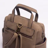 Mochila de diseño urbano en color caqui, confeccionada en cuero sintético con textura granulada y un bolsillo frontal de gamuza en tono más oscuro. Cuenta con manija superior, correas ajustables y bolsillos laterales.