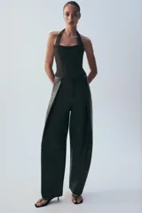 Top estilo corsé color beige, con escote recto, cuello halter y bajo asimétrico. Presenta costuras estructuradas frontales.