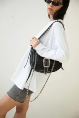 Cartera tipo baguette negra de cuero vacuno con textura tipo piel de cocodrilo. Tiene correa de cuero ajustable con detalles de tachas y cadena metálica plateada. El frente presenta un aplique de cuero con hebilla metálica plateada con tachas.