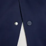 Campera tipo varsity New Balance, con cuerpo en azul marino y mangas en color crema. Presenta cierre frontal con botones a presión, cuello, puños y ruedo acanalados con rayas en contraste, y logo bordado en el pecho.