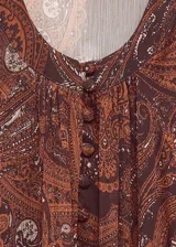 Vestido largo de corte evasé y diseño oversize, confeccionado en tejido semitransparente con estampado paisley en tonos rojizos y marrones. Presenta cuello escotado con cierre frontal, mangas largas con puños abullonados y forro interior.