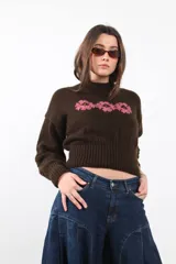Sweater tejido en lana merino color marrón chocolate, con diseño boxy, cuello redondo y detalles de flores bordadas en tono rosado en el pecho.