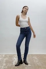 Jean skinny de tiro medio y calce ajustado, confeccionado en denim azul con leve elasticidad. Cuenta con diseño de cinco bolsillos, cierre frontal con botón y presillas en la cintura.
