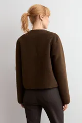 Chaqueta reversible de corte recto con cierre frontal de cremallera. Presenta un lado en acabado de gamuza negra y el reverso en tejido de textura tipo corderito color marrón chocolate, con cuello redondo y bolsillos frontales.