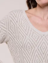 Buzo tejido de calce relajado, color beige, con escote en V y trama de punto calado con patrón de rombos. Cuenta con mangas largas de hombros caídos, ruedo y puños con acabado acanalado.