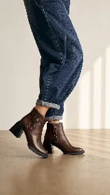 Bota corta de cuero marrón con diseño de paneles laterales texturizados. Presenta un taco ancho cuadrado en color negro y suela de plataforma baja, ofreciendo un estilo moderno y estable.