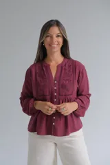 Blusa de manga larga color bordó con cuello mao y cierre frontal de botones. Presenta detalles de bordados florales y calados en el frente, con un corte holgado y puños elásticos.