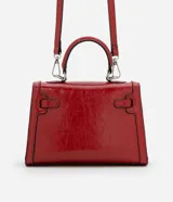 Cartera pequeña de poliuretano color rojo, con diseño estructurado, asa superior rígida y cierre frontal con herraje metálico.