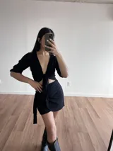 Top negro de tela slab con escote profundo en V y lazo frontal ajustable. Presenta mangas cortas y un diseño de corte cropped.