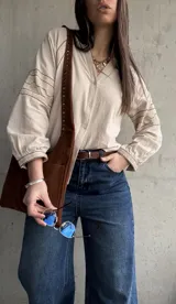 Camisa beige de inspiración boho con detalles bordados en mangas y puños, cuello en V con botones frontales y mangas largas abullonadas.