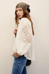 Camisa blanca de manga larga con detalles de encaje guipure en el pecho y las mangas, cuello en V y corte holgado.