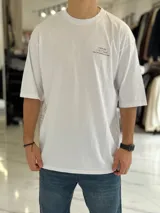 Remera oversize color beige, con mangas cortas y cuello redondo. Presenta un estampado tipográfico en la espalda con la frase "There are no facts, only interpretations" y otros detalles de diseño.