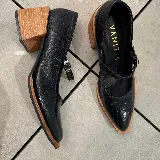Zapato tipo Mary Jane de cuero vacuno con textura grabada, color marrón oscuro. Presenta una puntera cuadrada, taco bloque de madera y una tira con hebilla metálica sobre el empeine.