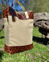 Bolso tipo shopper de lona color beige con apliques de cuero con estampado animal print y manijas doradas.