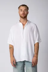 Camisa blanca de manga corta con cuello camisero y botones frontales. Presenta un corte oversize y confección en tela ligera.