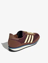 Zapatillas Adidas modelo SL 72 OG, con diseño retro de caña baja. Presentan un empeine de nailon en tono bordó con refuerzos de gamuza en color marrón, icónicas tres tiras laterales en color crema y detalles en piel. Incluyen una mediasuela de EVA con una franja azul y suela de goma dentada.