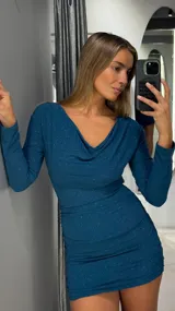 Vestido corto de manga larga en color azul petróleo con acabado brillante tipo lurex. Presenta un escote drapeado y diseño ajustado con frunces laterales en la falda.