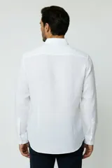 Camisa blanca de manga larga, con cuello camisero, cierre frontal de botones y un bolsillo aplicado en el pecho.