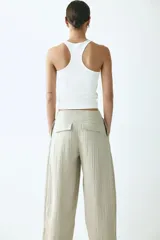 Pantalón tobillero de tiro alto en tejido arrugado color beige, con cierre de botón, bolsillos laterales y bajo ajustable con cordón.