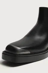Botas Chelsea de cuero negro con paneles elásticos laterales, suela gruesa y puntera redonda reforzada con una pieza metálica plateada.