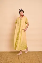 Vestido tipo túnica largo de lino color amarillo, de manga corta, con bolsillos laterales y detalle de volados en la botonera frontal.