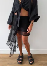 Falda corta negra de encaje con diseño irregular y un volante largo asimétrico en un lateral. Posee cintura elástica y forro interior.