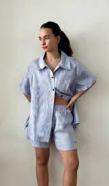 Conjunto de dos piezas color celeste claro, compuesto por una camisa de manga corta con cuello y botones negros, y un short a juego con elástico en la cintura.