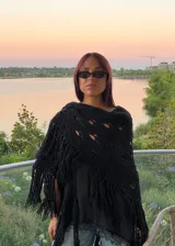 Ruana tejida artesanalmente en lana merino, de color negro, con diseño calado y terminación de flecos largos en los bordes.