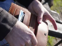 Billetera de cuero color marrón con costuras decorativas en los bordes, cierre con broche a presión y bolsillo interno con cierre.