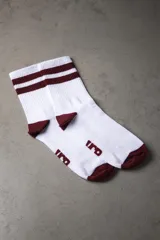 Medias deportivas de caña media, color blanco con dos franjas horizontales bordó en la parte superior, puntera y talón en color bordó, y logo estampado en el empeine.
