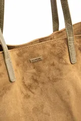 Bolso tipo tote de gran tamaño confeccionado en material sintético con acabado efecto gamuza en color tostado. Presenta doble asa larga en tono contrastante y placa metálica pequeña con logo de la marca en la parte frontal.
