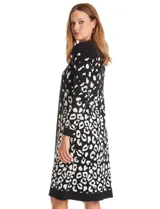 Vestido midi de tejido de punto con diseño integrado que simula un conjunto de vestido y cárdigan. Presenta un color base negro con detalles geométricos en blanco en las mangas y el ruedo. Posee escote redondo y mangas largas.