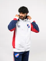 Campera deportiva Umbro del Club Nacional de Football, con cierre frontal, capucha ajustable con cordones y diseño en bloques de color azul, celeste y blanco. Presenta el logo de la marca y el escudo del club bordados en el pecho.