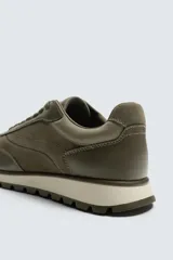 Zapatilla deportiva color verde militar, con parte superior de múltiples piezas que combinan piel y serraje. Presenta horma redonda y suela dentada en color crema con base marrón.