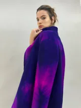Tapado de lana merino afieltrada con diseño artesanal teñido en tonos violeta y fucsia. Presenta cuello elevado, cierre frontal con broches ocultos, bolsillos laterales y un corte ligeramente más largo en la parte trasera.