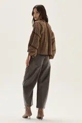 Blusa de color marrón con estampado de rayas verticales y pequeñas flores blancas. Presenta cuello redondo con lazo de ajuste, cierre frontal con botones y mangas largas abullonadas con detalles de encaje calado y puños ajustables con lazo.