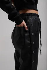 Pantalón negro de cuero sintético con bolsillos laterales y botones metálicos a presión en los laterales.