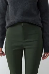 Pantalón de tiro medio y fit slim, color verde militar. Confeccionado en tejido elasticado, no presenta bolsillos visibles y cuenta con cierre frontal oculto.