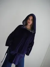 Buzo tipo canguro oversize de tela plush, color azul claro. Presenta capucha, cierre frontal parcial con cordón turquesa y bolsillos canguro frontales. Las mangas son largas y abullonadas con puños ajustados.