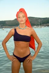 Bikini de tela lúrex color violeta con acabado brillante. El corpiño es tipo top de un solo hombro con hebilla metálica decorativa en el tirante. La bombacha es de corte vedetina.
