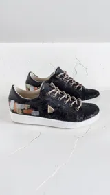 Championes de cuero negro jaspeado con suela blanca y cordones beige, con detalles pintados a mano en el talón y aplique metálico triangular.