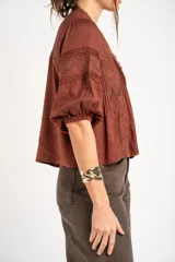 Blusa de viscosa y lino color crudo, con cuello en V, mangas tres cuartos abullonadas e inserciones de encaje floral y detalles plisados frontales.