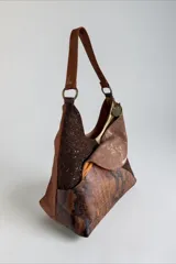 Cartera de cuero de diseño envolvente y líneas orgánicas, con combinación de texturas, apliques y estampado de serpiente, asa de hombro y bolsillos exteriores.