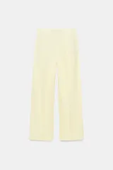Pantalón de tiro medio de pierna ancha color amarillo pastel, confeccionado con mezcla de lino. Cuenta con bolsillos laterales ocultos, pliegues delanteros y cierre frontal con cremallera, botón y ganchos metálicos.