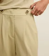 Pantalón zanahoria de cintura alta color beige, confeccionado en tejido piqué con viscosa sostenible. Cuenta con cierre tradicional, cintas con botones en la cintura, pliegues y dobladillo en el bajo.