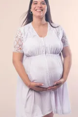Camisón maternal blanco de algodón elastizado, con escote redondo, mangas cortas de puntilla y detalle de puntilla en los hombros. Presenta cierre frontal con botones y elástico bajo el busto para mayor sujeción.